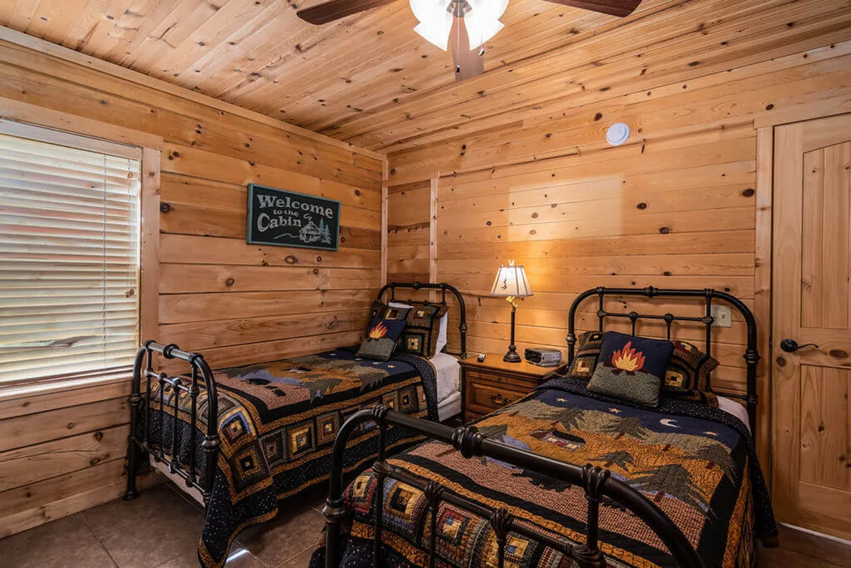 A twin bedroom with two neatly made beds against wooden wall panels, a welcoming sign above the nightstand, and a lamp providing a soft, inviting glow. The room exudes a family-friendly atmosphere, perfect for children or friends traveling together.
