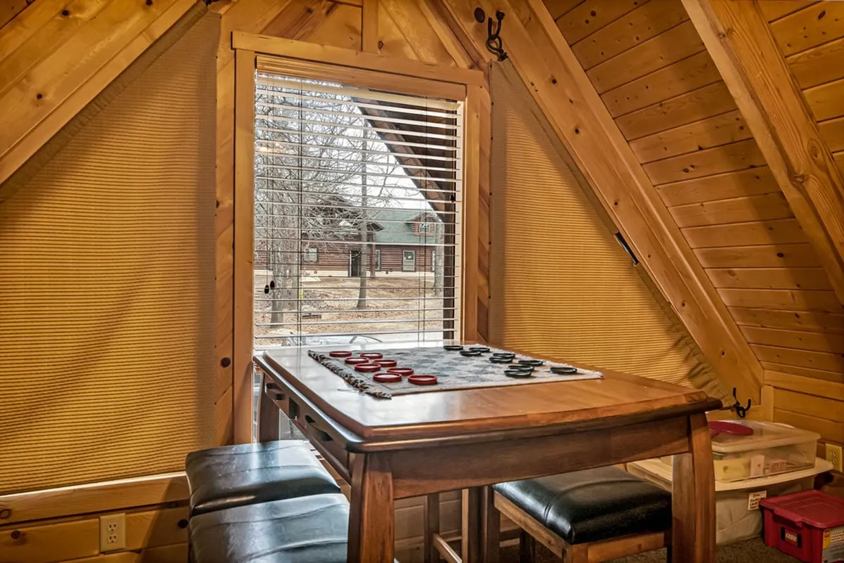 A cozy nook in the loft with a checkerboard game table, rustic wooden beams, and a large window offering a tranquil view. The area feels relaxed and welcoming, encouraging both imaginative play and quiet moments with family or friends.