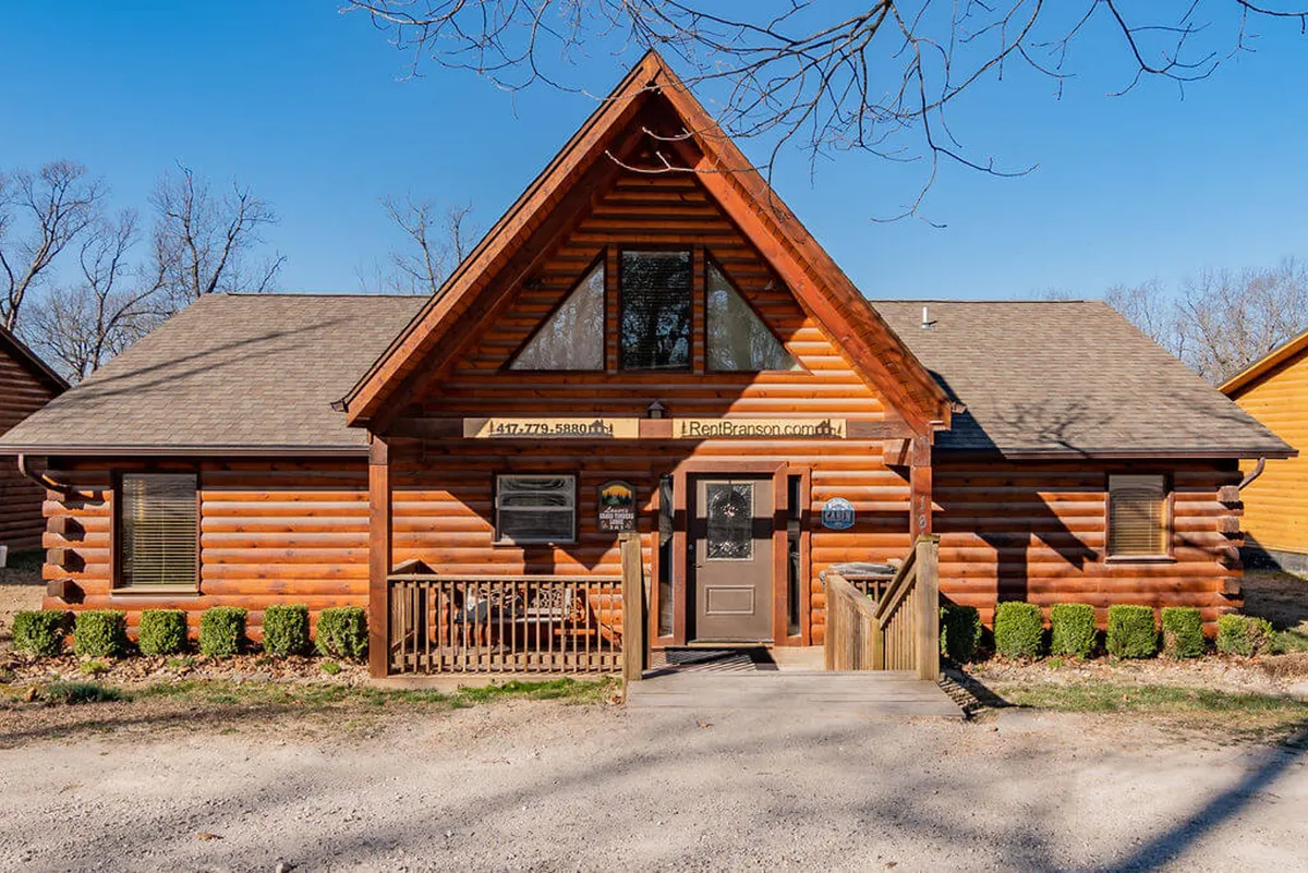 A welcoming log cabin with large front windows, wooden steps, and a rustic porch set among trees. The outdoor setting feels cozy and private, offering a personal retreat after a day of outdoor exploration for both guests and their pets.
