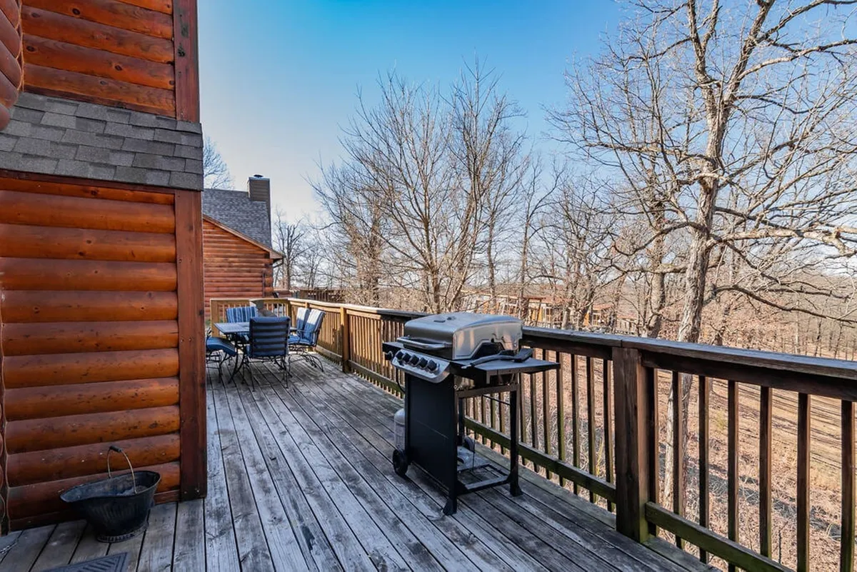 A welcoming outdoor space featuring a grill, dining table, and wooden deck surrounded by trees. The setup is ideal for barbecuing, al fresco meals, and enjoying nature in a relaxed atmosphere.
