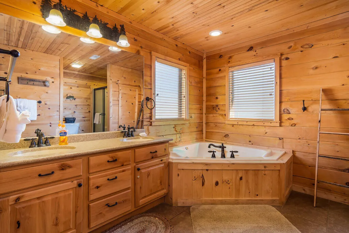 A spacious bathroom with a large bathtub, elegant wood cabinetry, mirrors, and warm lighting fixtures. The tranquil ambiance invites relaxation, reminiscent of a spa experience.
