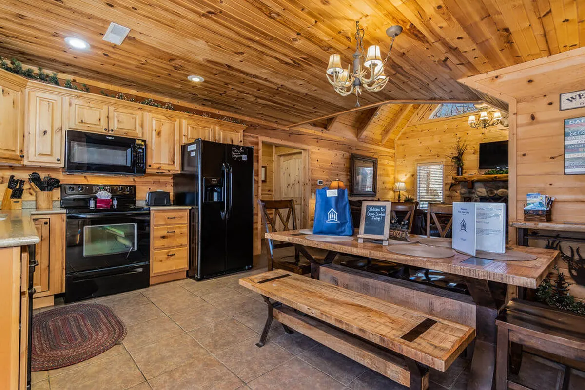 A warm, inviting kitchen and dining area featuring wooden cabinetry, modern appliances, a spacious dining table, and a stylish chandelier. The setup exudes a sense of togetherness, perfect for shared meals and lively conversation. Ample natural light brightens the space, making it feel both homely and celebratory.