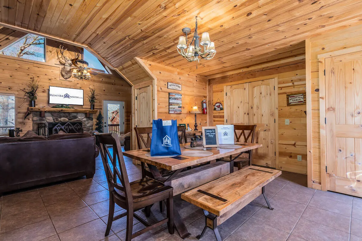 A cozy dining space with a wooden table set beneath an elegant chandelier, complemented by a nearby fireplace and rich wooden accents. The atmosphere is intimate and inviting, perfect for family meals, game nights, or evening conversations.
