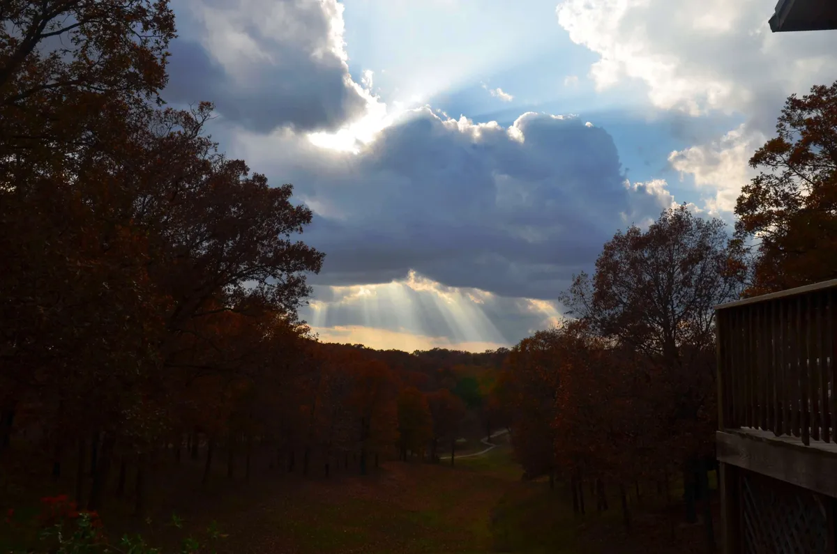 A tranquil scenic view with rays of sunlight breaking through the clouds, illuminating vibrant autumn foliage and a winding path in a peaceful valley. The image evokes the beauty and tranquility of nature, inviting exploration and leisurely walks.