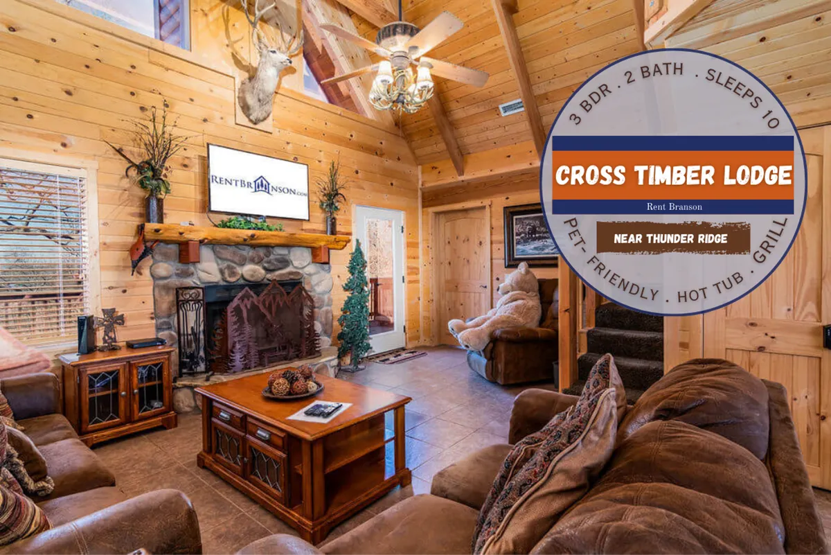 A welcoming living room with comfortable seating arranged around a prominent stone fireplace and wooden beams overhead. A television adds entertainment value, ideal for movie nights or catching the big game, while abundant natural light filters through the space.