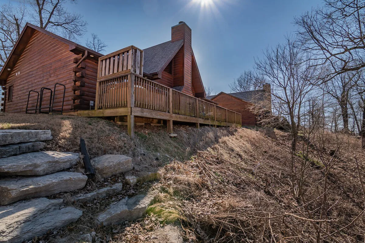 This cozy scene shows a charming wooden deck attached to a cabin, complete with stone steps and surrounded by greenery. It invites guests to relax outdoors, enjoy morning coffee, or gather for evening barbecues.