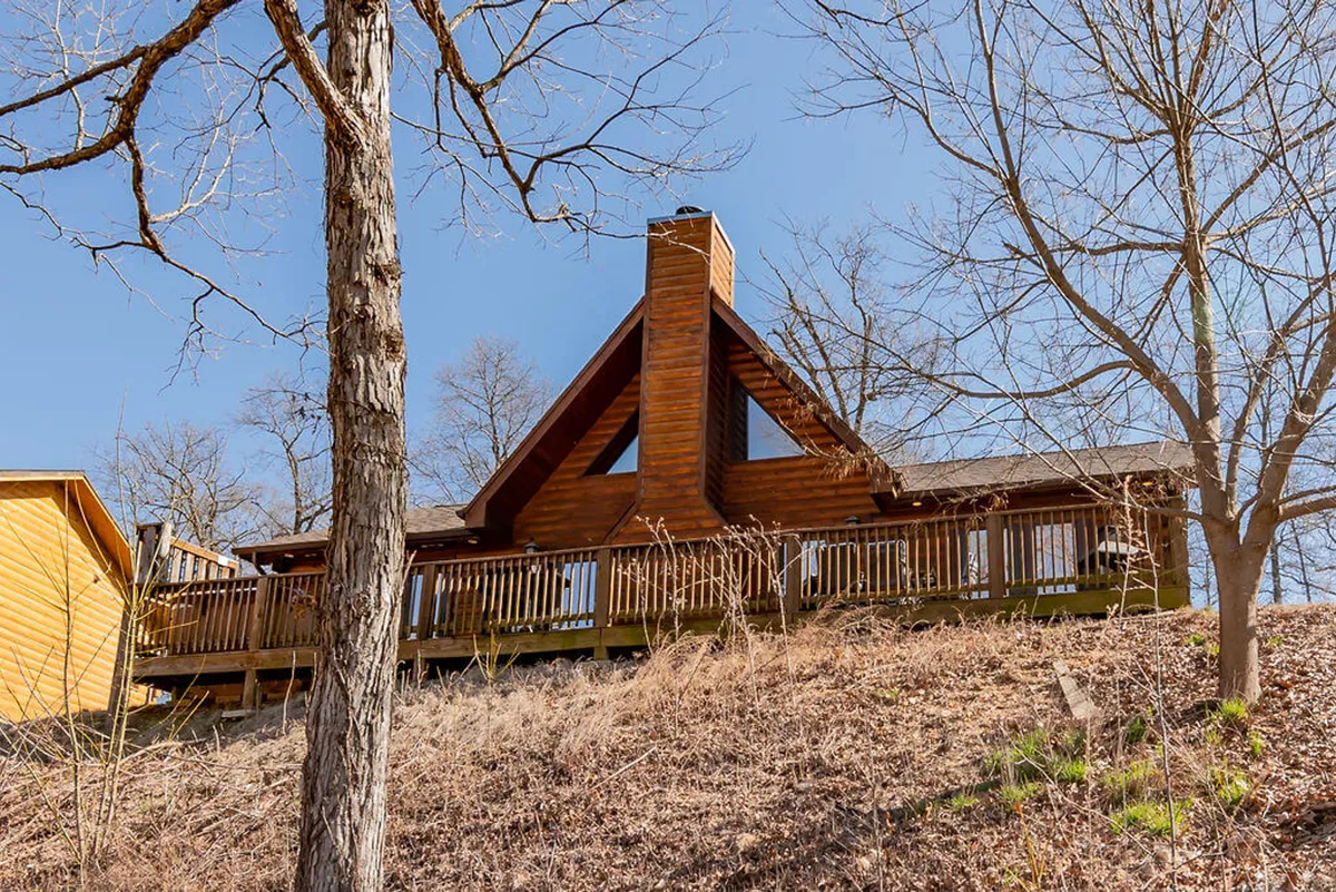 A welcoming wooden cabin with a stone chimney and a spacious deck framed by trees. The deck invites gatherings and relaxation, while the setting highlights the lodge’s blend of privacy and access to nature.
