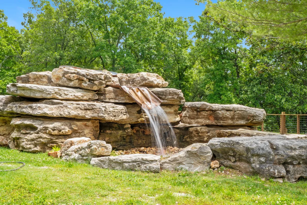 A serene natural waterfall cascades over rugged rocks surrounded by lush greenery, offering a peaceful and intimate setting that feels tucked away from the world. The gentle flow of the water and the vibrant flora create a tranquil atmosphere ideal for romantic escapes or quiet reflection.