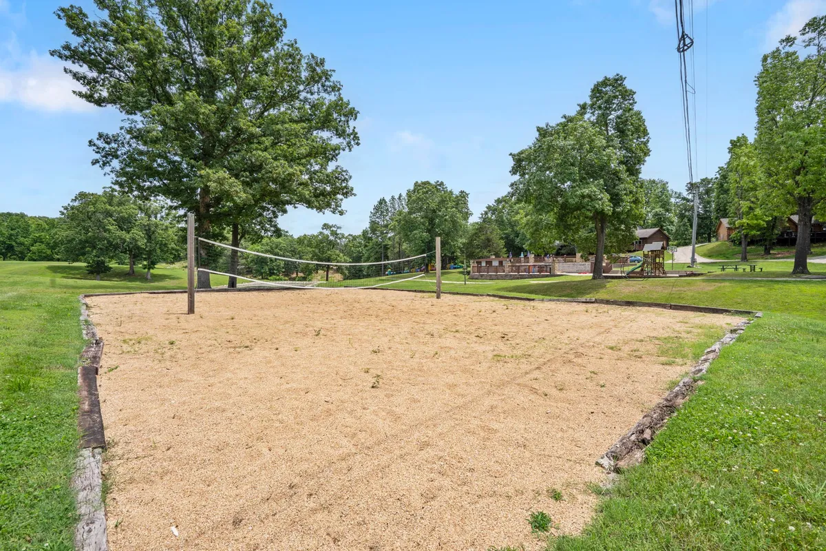 An outdoor volleyball court bordered by tall trees and neighboring structures, creating a laid-back setting for friendly group matches and social gatherings. The space suggests opportunities for active fun close to the lodge.